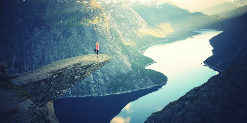 Person on a cliff edge overlooking a river valley to showcase wellness personas and achievement